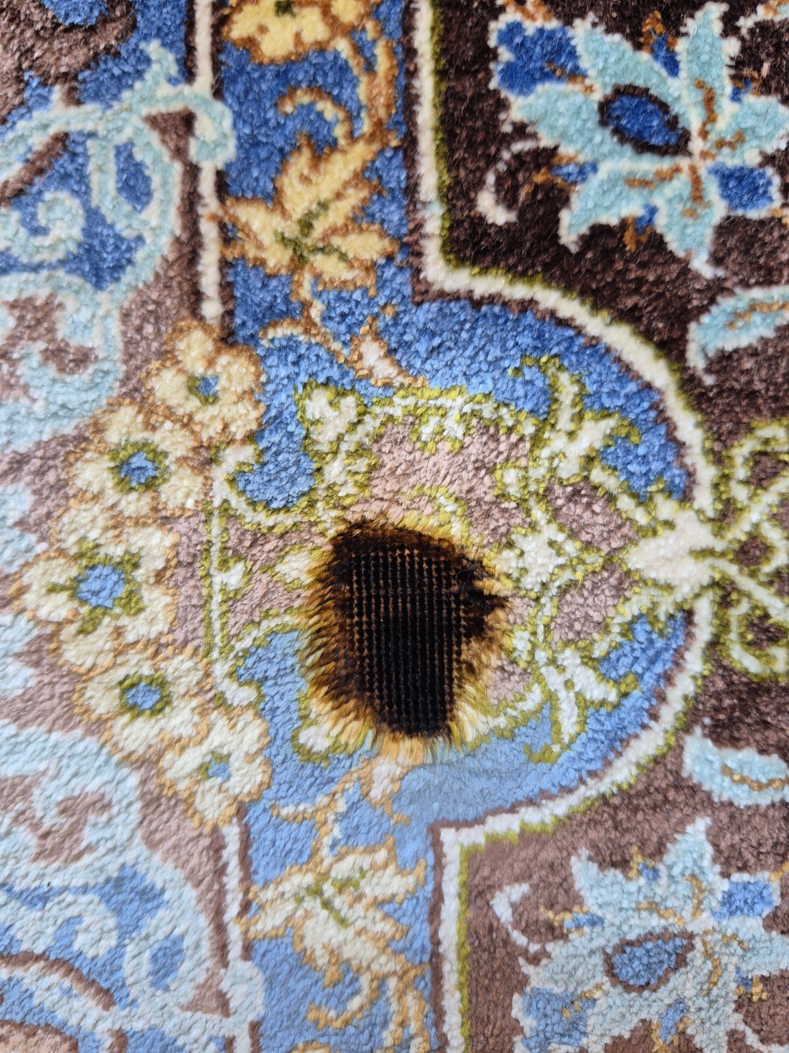 Burn hole in a silk Persian rug before repair, charred pile and exposed foundation
