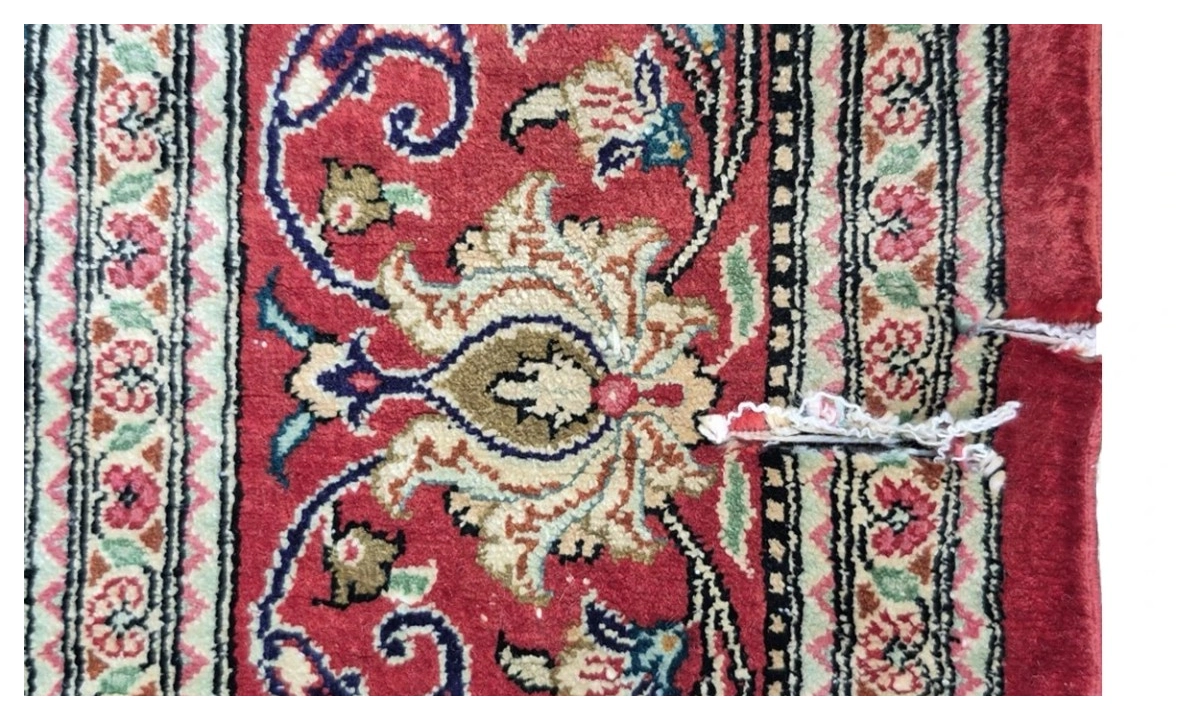 Red Persian rug edge before repair, side cord split with loose repair threads